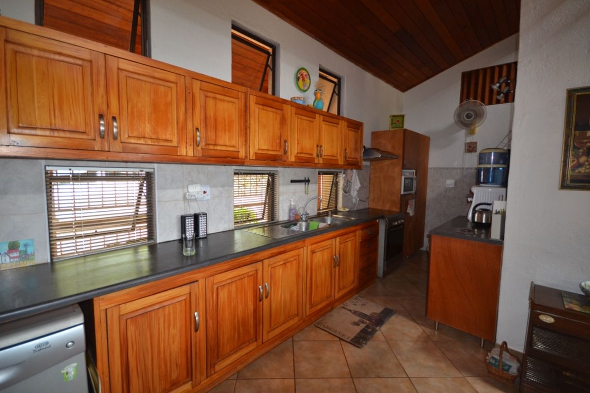 A functional kitchen featuring warm wooden cabinetry, dark laminate countertops, tiled flooring, and a vaulted timber ceiling with natural light from top-hung windows.