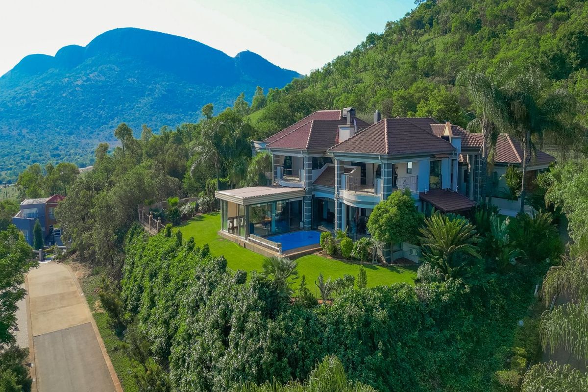 Aerial view of a luxury multi-story residence featuring a swimming pool, expansive patio, and landscaped gardens set against a scenic mountain backdrop.