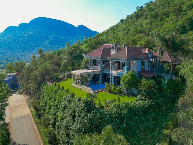 Aerial view of a luxury multi-story residence featuring a swimming pool, expansive patio, and landscaped gardens set against a scenic mountain backdrop.