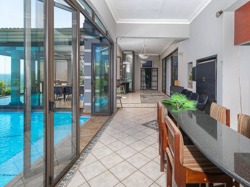 Spacious covered patio featuring tiled flooring, built-in braai, and direct access to the swimming pool through large sliding glass doors.