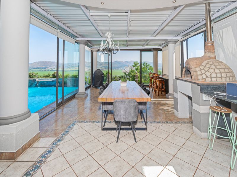 Spacious covered patio featuring a built-in pizza oven, tiled flooring, and large sliding glass doors overlooking the swimming pool and scenic landscape.