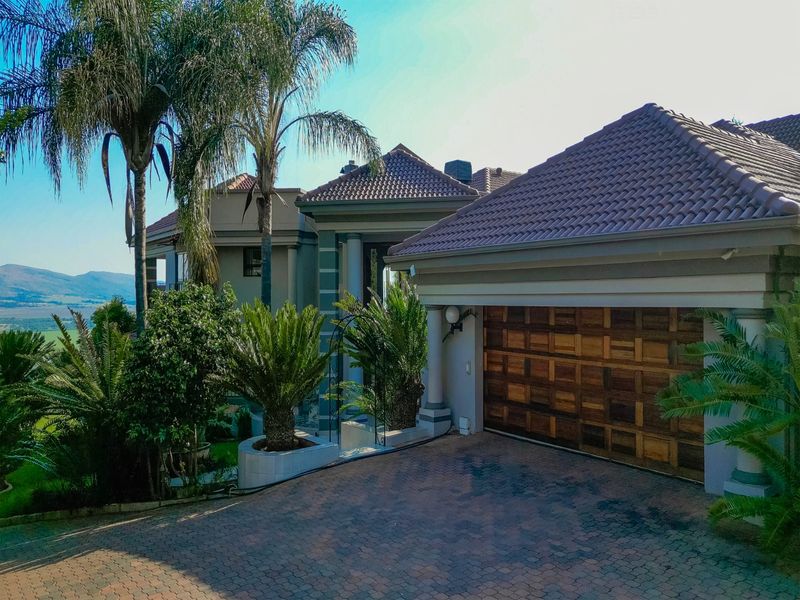 Front elevation of a multi-story residence featuring a paved driveway, wooden garage door, and established garden with scenic mountain views.