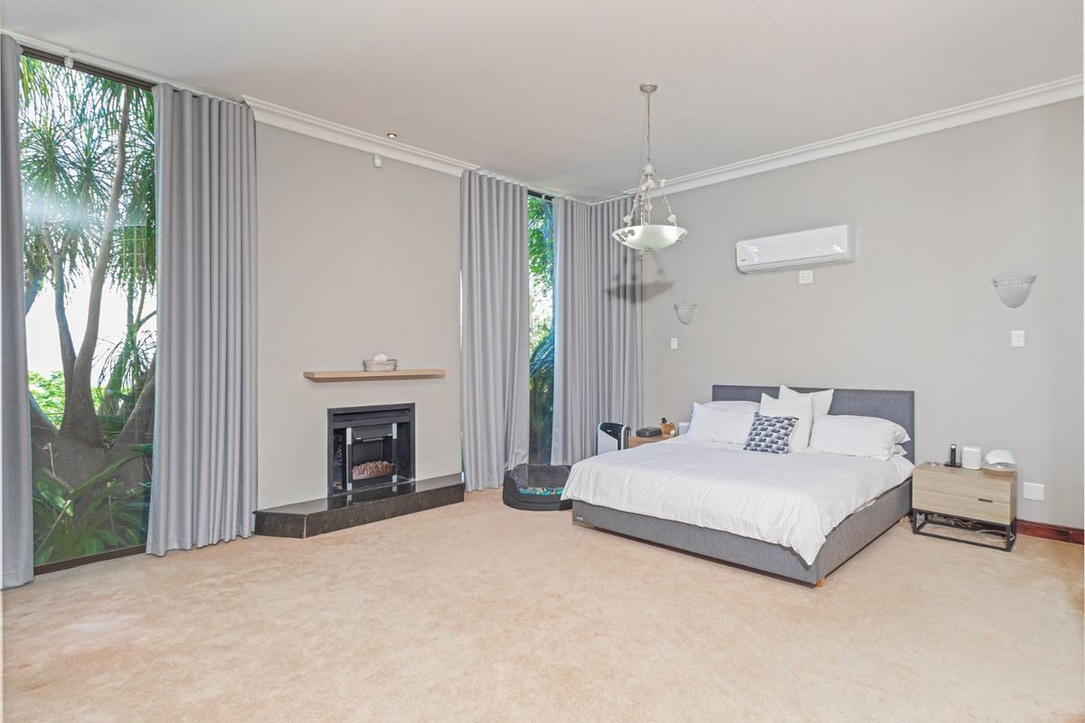 Spacious bedroom featuring a built-in fireplace, floor-to-ceiling windows, wall-mounted air conditioning, and neutral carpeting.