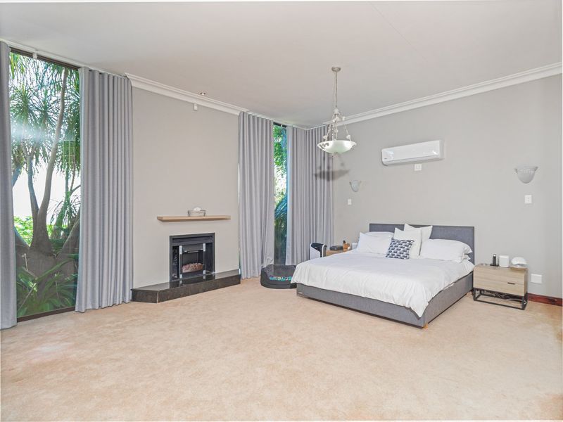 Spacious bedroom featuring a built-in fireplace, floor-to-ceiling windows, wall-mounted air conditioning, and neutral carpeting.