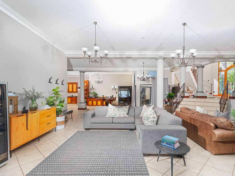 Spacious open-plan living area featuring tiled floors, decorative columns, and elegant chandeliers, with a seamless flow towards the kitchen and staircase.