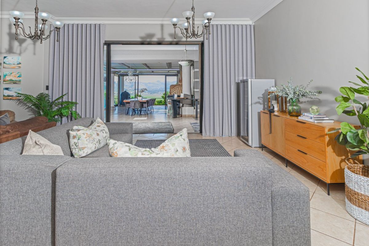 Spacious living room featuring tiled flooring, elegant chandeliers, and large sliding glass doors that open to an outdoor entertainment area with scenic views.