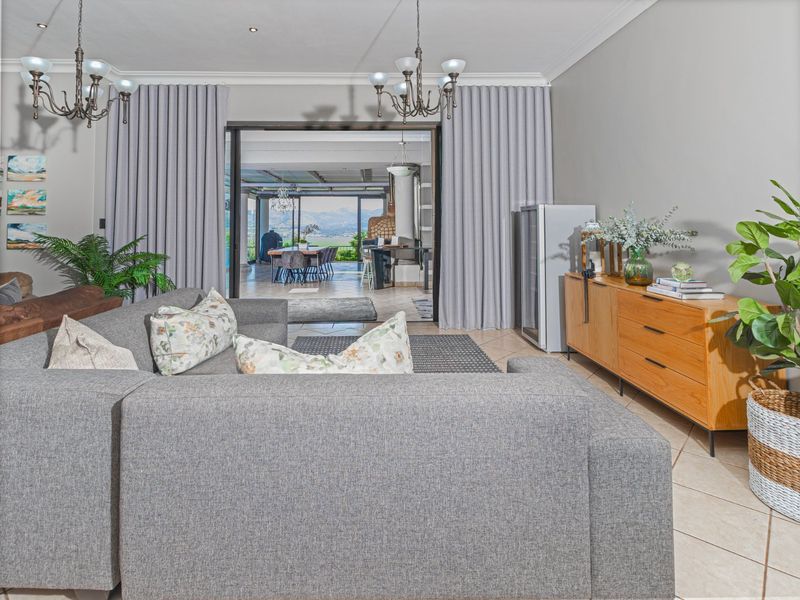 Spacious living room featuring tiled flooring, elegant chandeliers, and large sliding glass doors that open to an outdoor entertainment area with scenic views.