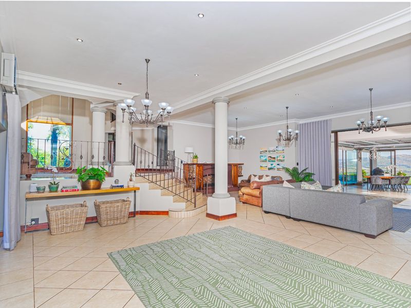 Spacious open-plan living area featuring tiled floors, decorative columns, a built-in bar, and a grand staircase with wrought iron detailing.