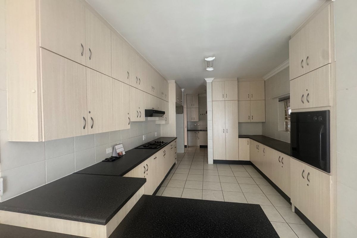 Spacious kitchen featuring extensive built-in cabinetry, dark laminate countertops, a built-in oven, gas hob, and tiled flooring throughout.