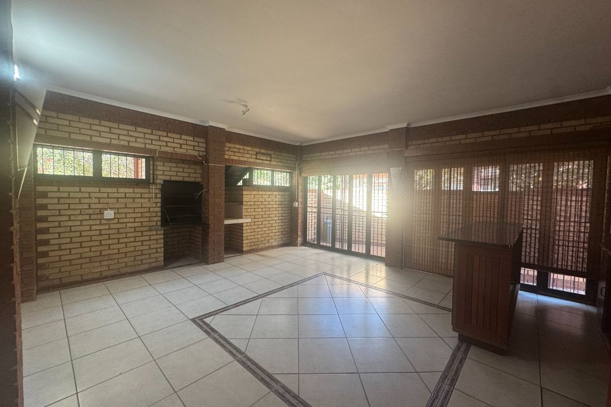 Spacious living area featuring exposed brick walls, built-in braai, and tiled flooring with direct access to the outdoor area through sliding glass doors.