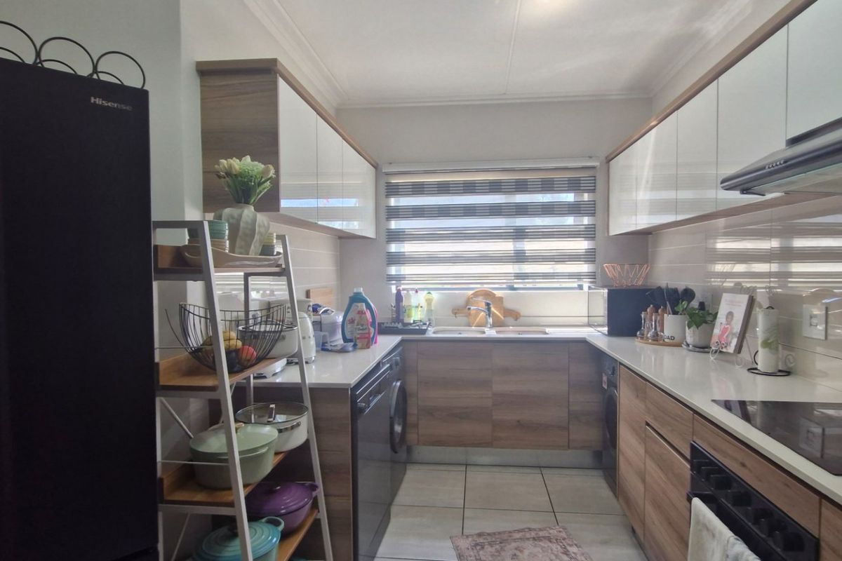 Modern galley-style kitchen featuring wood-finish cabinetry, stone countertops, integrated hob, extractor fan, and tiled backsplash with ample storage space.