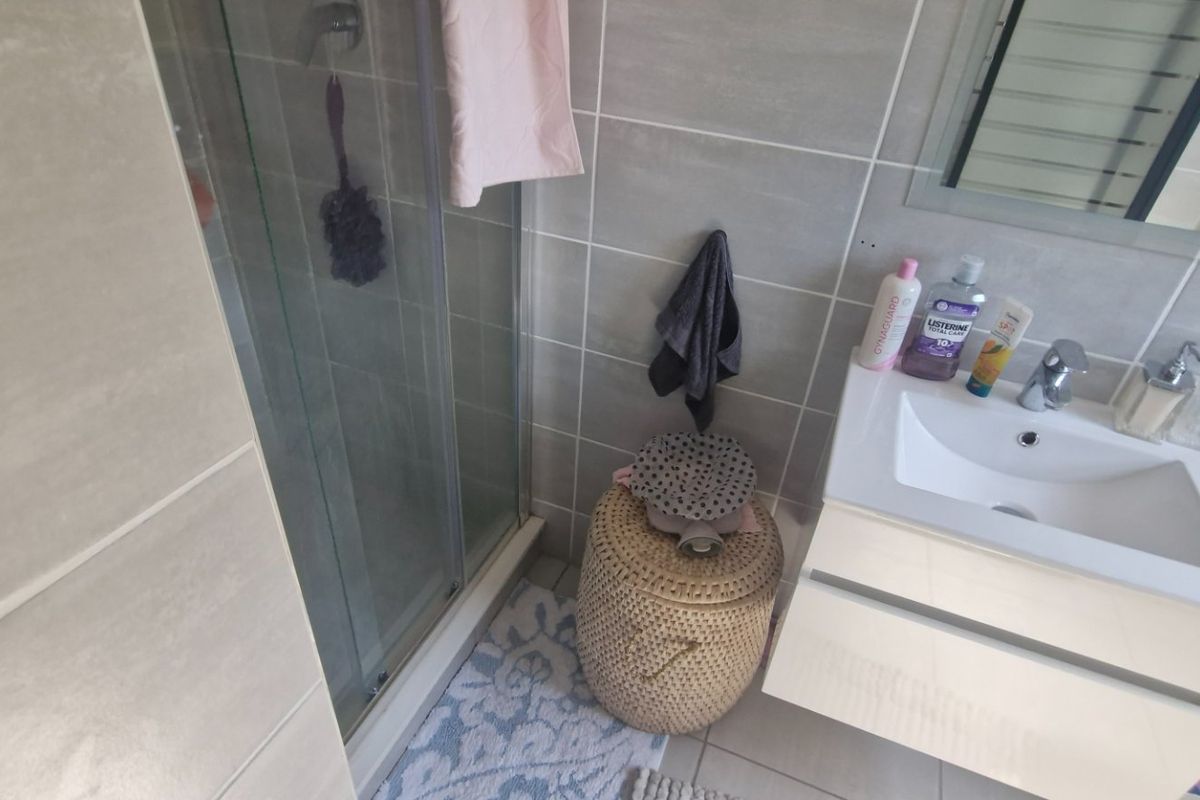 A modern bathroom featuring a glass shower enclosure, a sleek wall-mounted vanity with a ceramic basin, and neutral grey wall tiling.