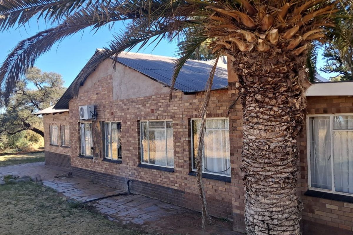 Rear view of a face brick farmhouse featuring a corrugated metal roof, stone paved walkway, and exterior-mounted air conditioning unit.