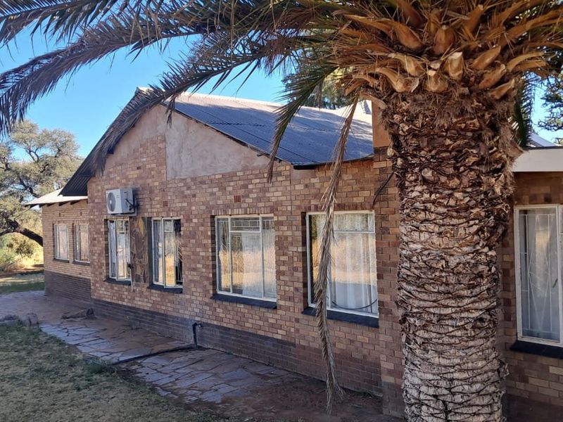Rear view of a face brick farmhouse featuring a corrugated metal roof, stone paved walkway, and exterior-mounted air conditioning unit.