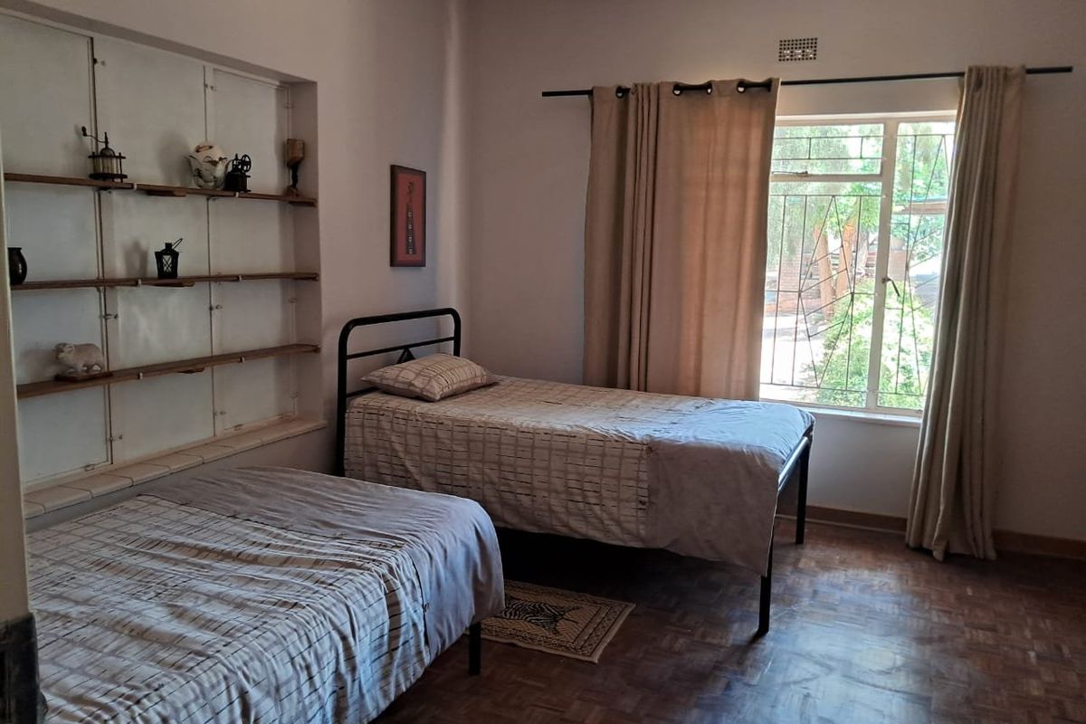 A bedroom featuring parquet flooring, built-in wall shelving, and a window with security bars, offering a functional space with potential for cosmetic updates.