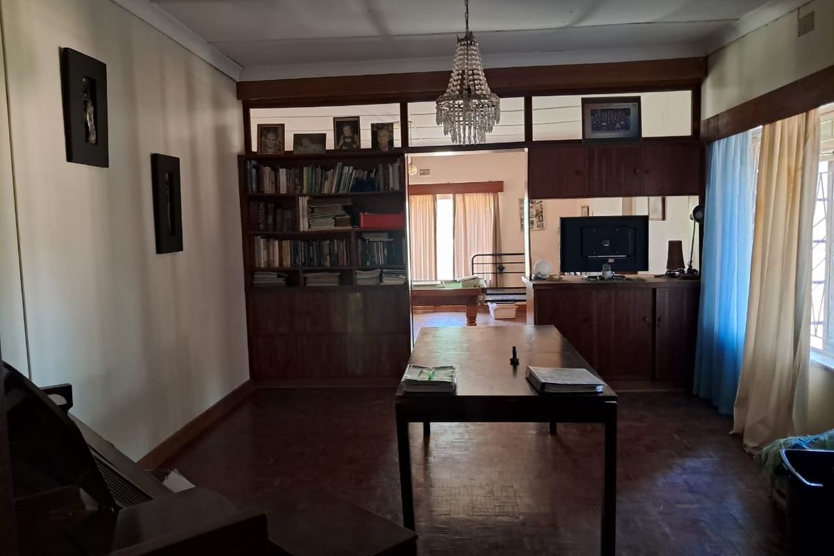 A living area featuring traditional parquet flooring, built-in wooden cabinetry, and a classic chandelier, offering a dated but functional space with potential for modernization.