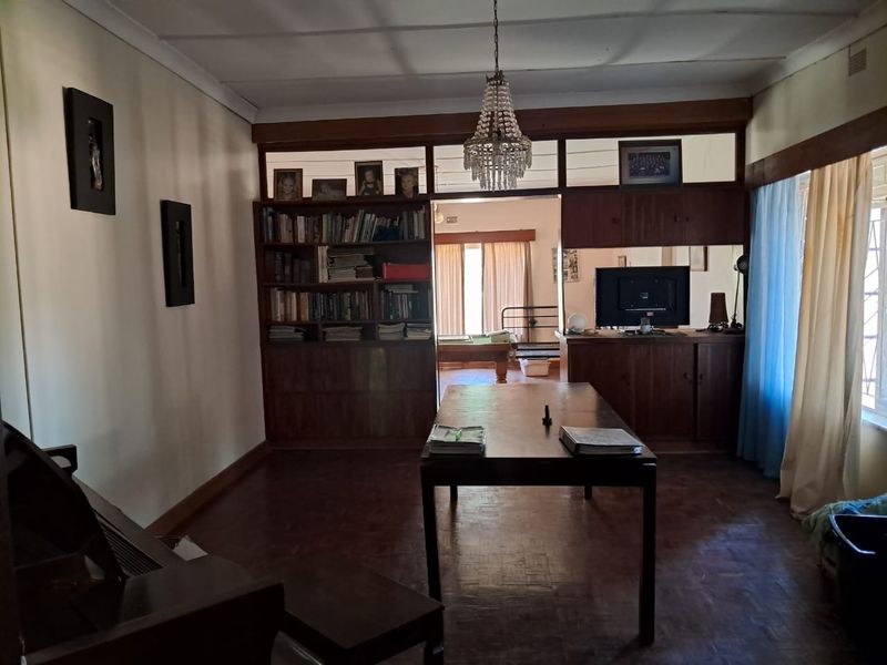 A living area featuring traditional parquet flooring, built-in wooden cabinetry, and a classic chandelier, offering a dated but functional space with potential for modernization.