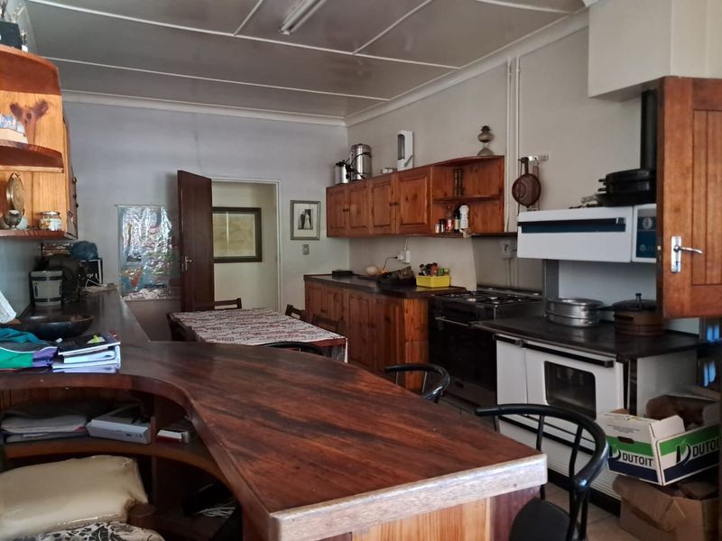 A rustic farm-style kitchen featuring wooden cabinetry, a built-in oven, and a large breakfast bar, offering a functional layout with potential for modernization.