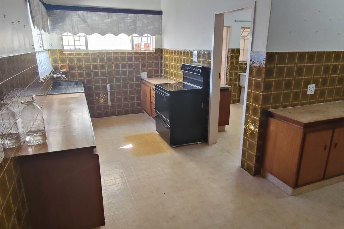A dated kitchen featuring original brown tiled splashbacks, wooden cabinetry, and a freestanding stove, offering significant potential for a modern renovation.