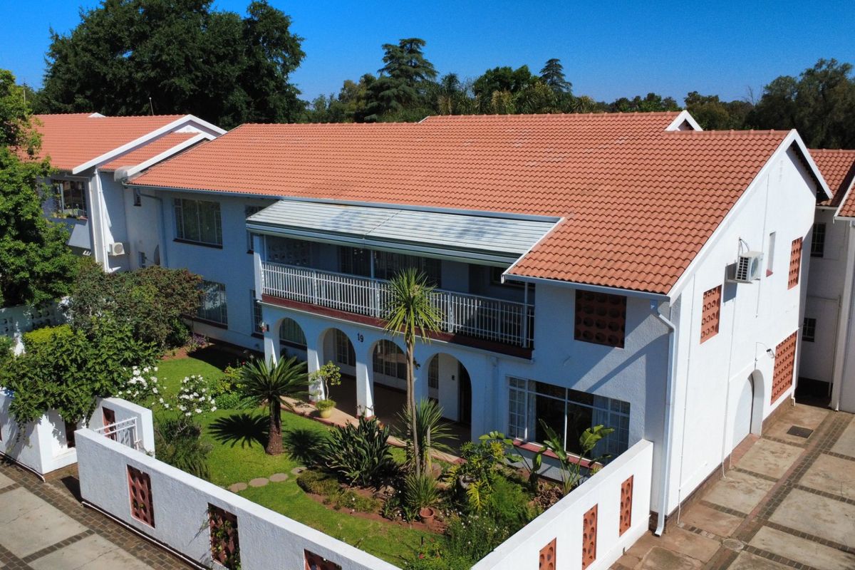 Aerial view of a townhouse complex featuring a tiled roof, balcony, arched entrance, and a well-maintained garden with a paved driveway.