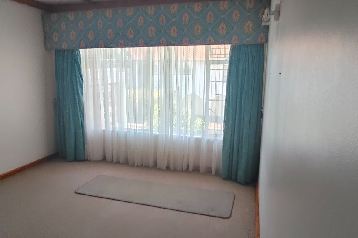 A spacious, empty bedroom featuring neutral carpeting and a large window with decorative pelmet and curtains.