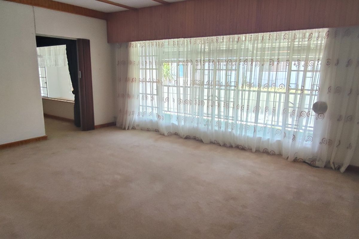 An empty, dated living room featuring carpet flooring, timber ceiling detailing, and a large sliding glass door providing access to the exterior.