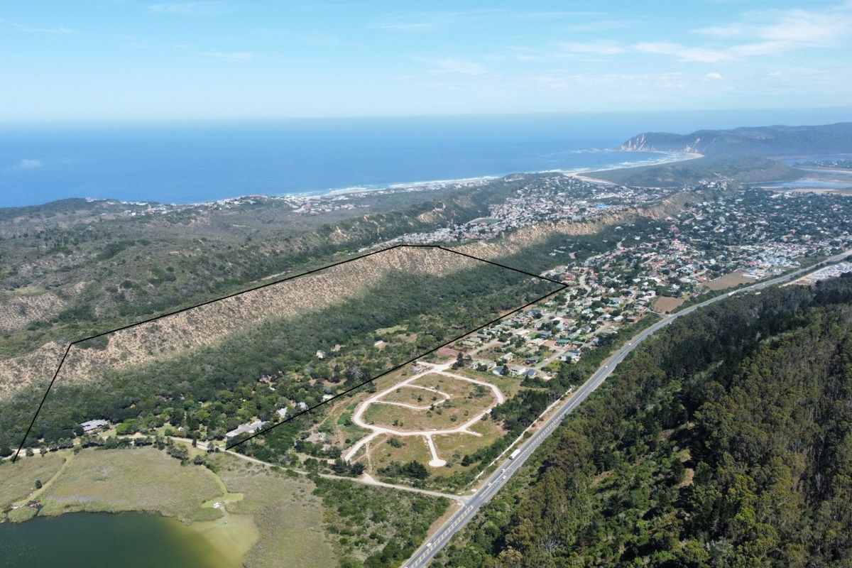 Aerial view of a large coastal land parcel with established road infrastructure, bordering a residential area and natural landscape.