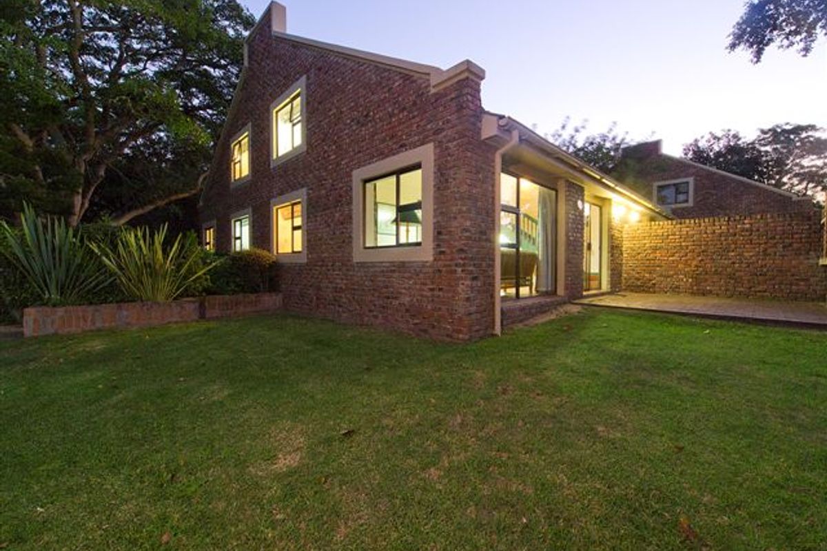 A rear view of a commercial property featuring exposed brickwork, large windows, and a well-maintained lawn area.
