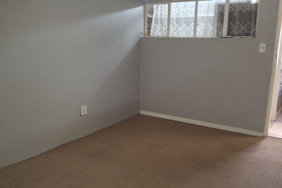 An empty bedroom featuring carpet flooring, neutral grey walls, and an internal window providing natural light from the adjacent hallway.