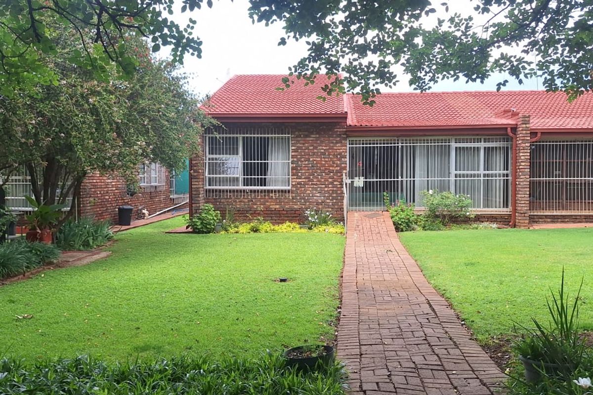 A well-maintained rear exterior view of a face brick apartment featuring a tiled roof, security bars on windows, and a paved garden walkway.