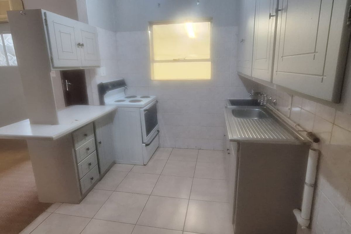 A functional, dated kitchen featuring tiled flooring, built-in cabinetry, a stainless steel sink, and a freestanding stove, offering potential for modern renovation.