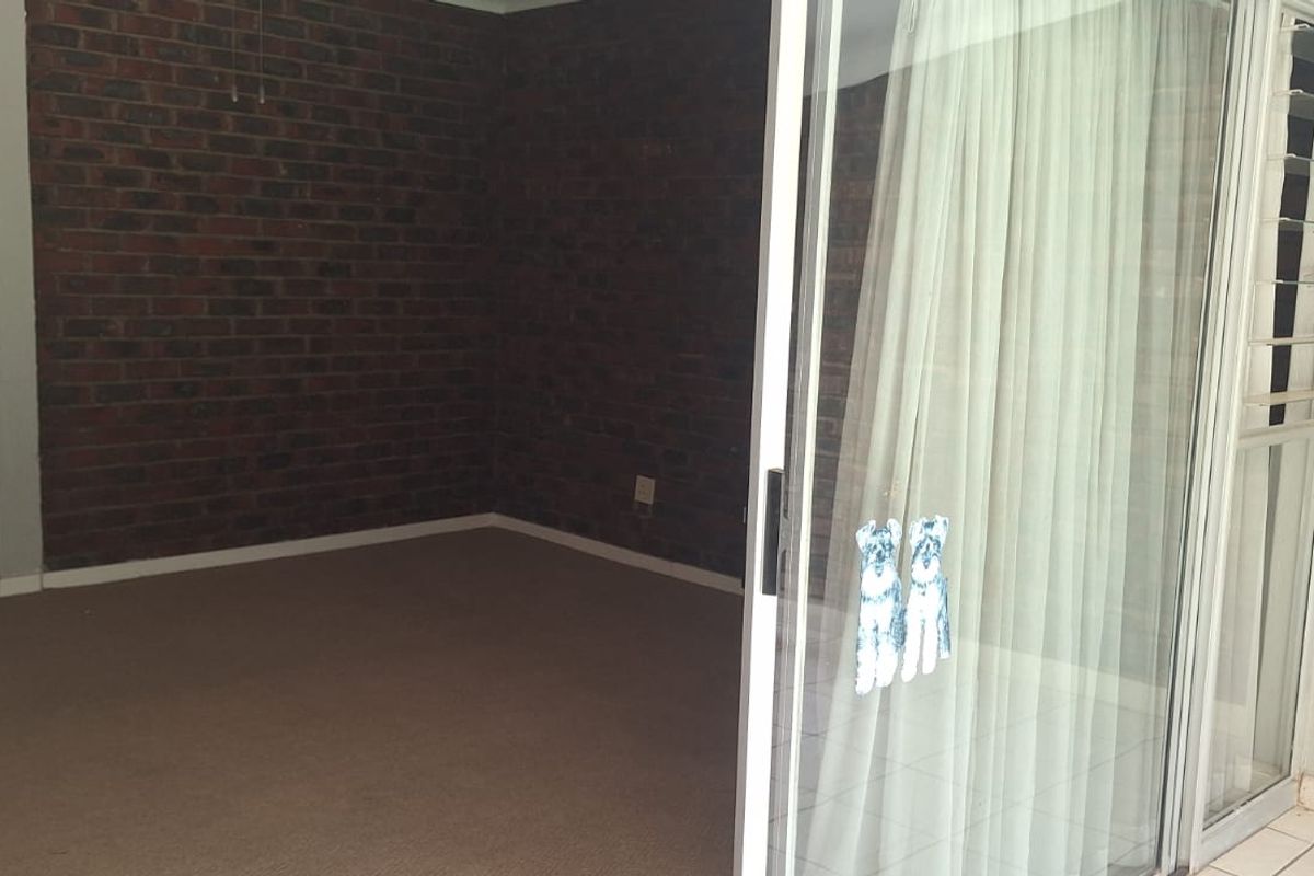 An empty living room featuring an exposed brick wall and large sliding glass doors leading to an outdoor area.