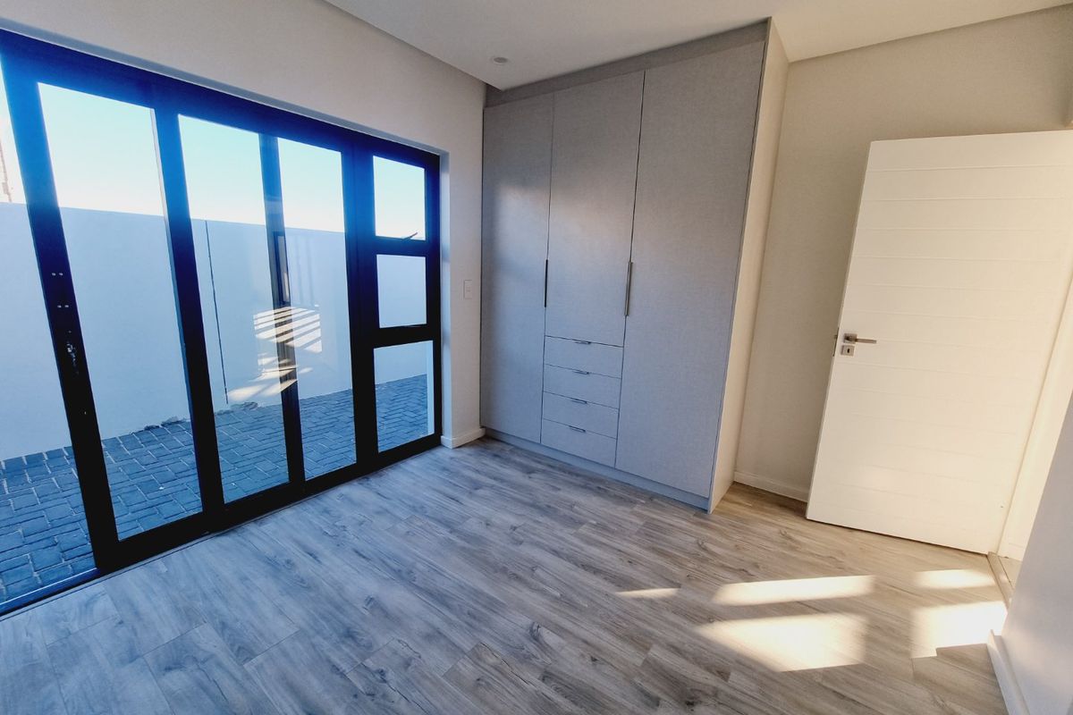 A bright, modern bedroom featuring light wood-look laminate flooring, a spacious built-in wardrobe, and large sliding glass doors leading to an outdoor area.