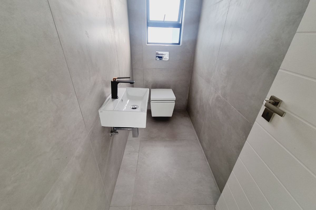 A modern, minimalist guest bathroom featuring large format grey tiles, a wall-mounted basin with a black mixer tap, and a wall-hung toilet.