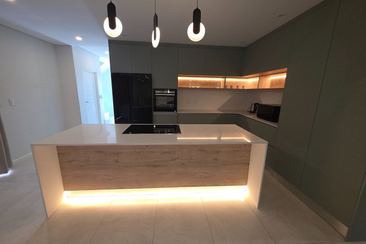 Modern kitchen featuring a central island with induction cooktop, quartz countertops, integrated cabinetry, and ambient under-cabinet and pendant lighting.
