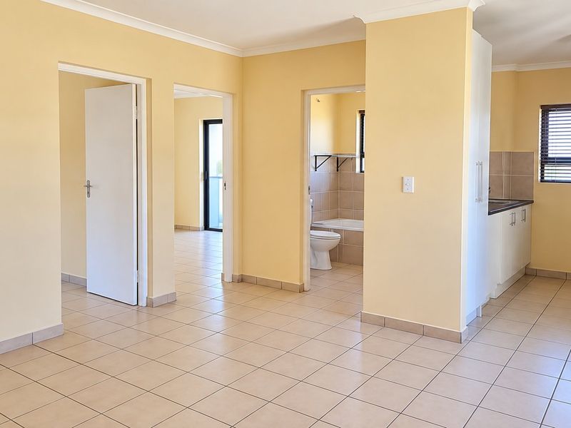 An open-plan living and kitchen area featuring tiled flooring, neutral walls, and direct access to adjacent rooms and a bathroom.