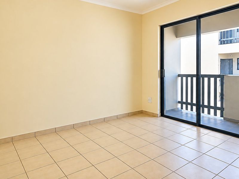 An empty bedroom featuring neutral tiled flooring and a large sliding glass door providing access to a private balcony.