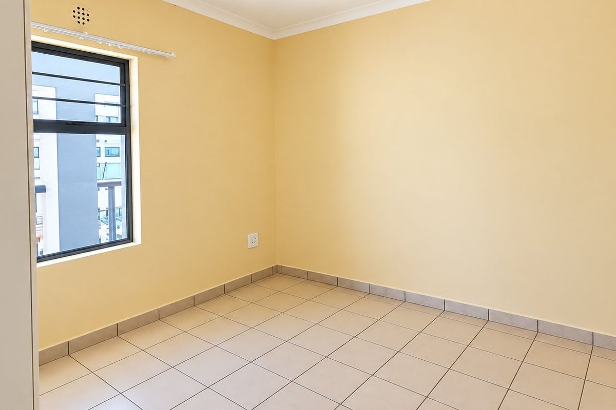 A clean, empty bedroom featuring neutral yellow walls, tiled flooring, and an aluminium-framed window with security bars.