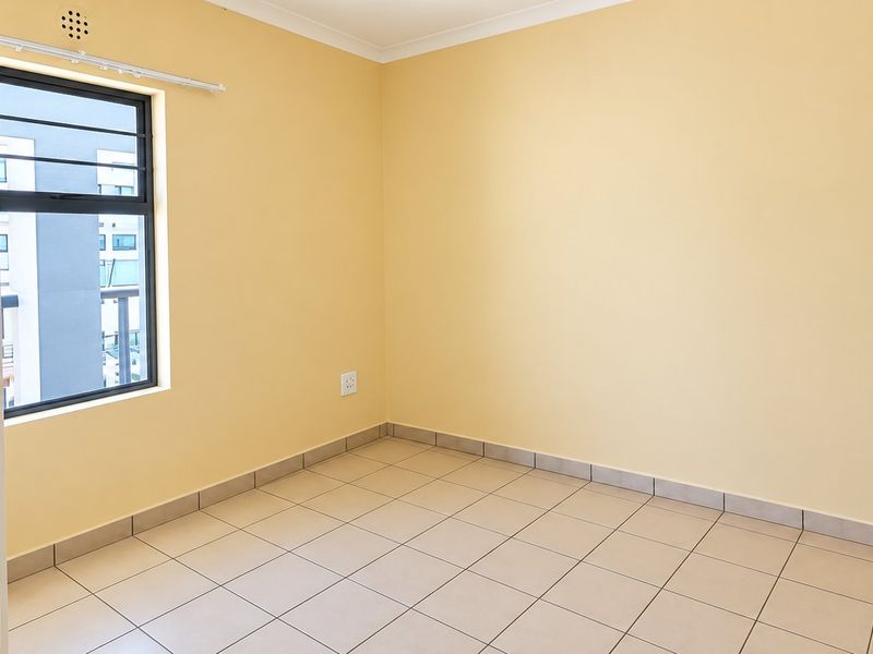 A clean, empty bedroom featuring neutral yellow walls, tiled flooring, and an aluminium-framed window with security bars.