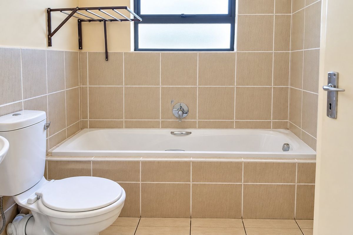A clean, functional bathroom featuring a built-in bathtub, tiled walls and flooring, and a wall-mounted towel rack.