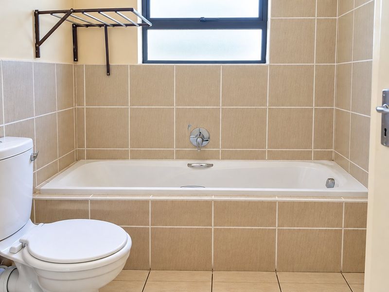 A clean, functional bathroom featuring a built-in bathtub, tiled walls and flooring, and a wall-mounted towel rack.