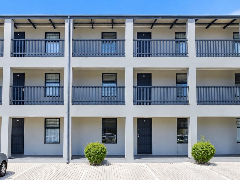 A well-maintained multi-story apartment building facade featuring uniform balconies, secure external access doors, and a paved ground-level parking area.