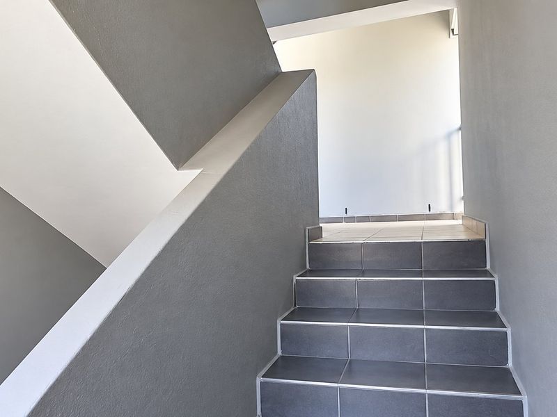 A clean, modern staircase featuring grey tiled steps and a solid, minimalist balustrade in a neutral interior hallway.