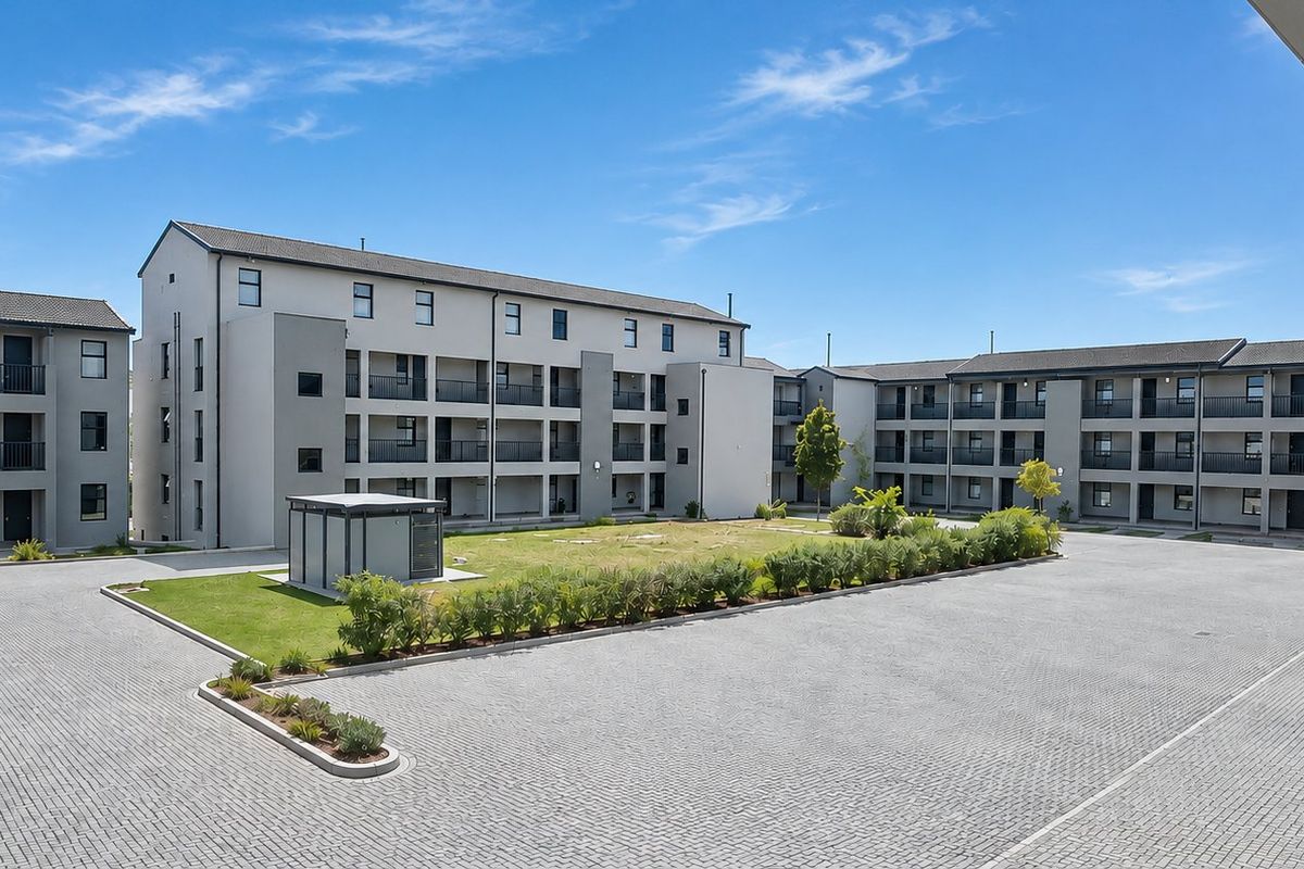 A wide-angle view of the apartment complex exterior, featuring paved parking areas, communal garden spaces, and multi-story residential blocks with balconies.