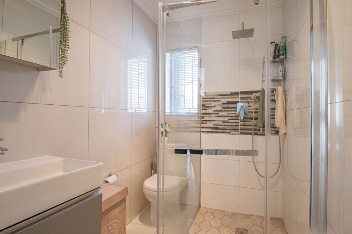 Modern bathroom featuring a glass-enclosed shower with a rain shower head, a wall-mounted basin, and stylish mosaic tile accents.