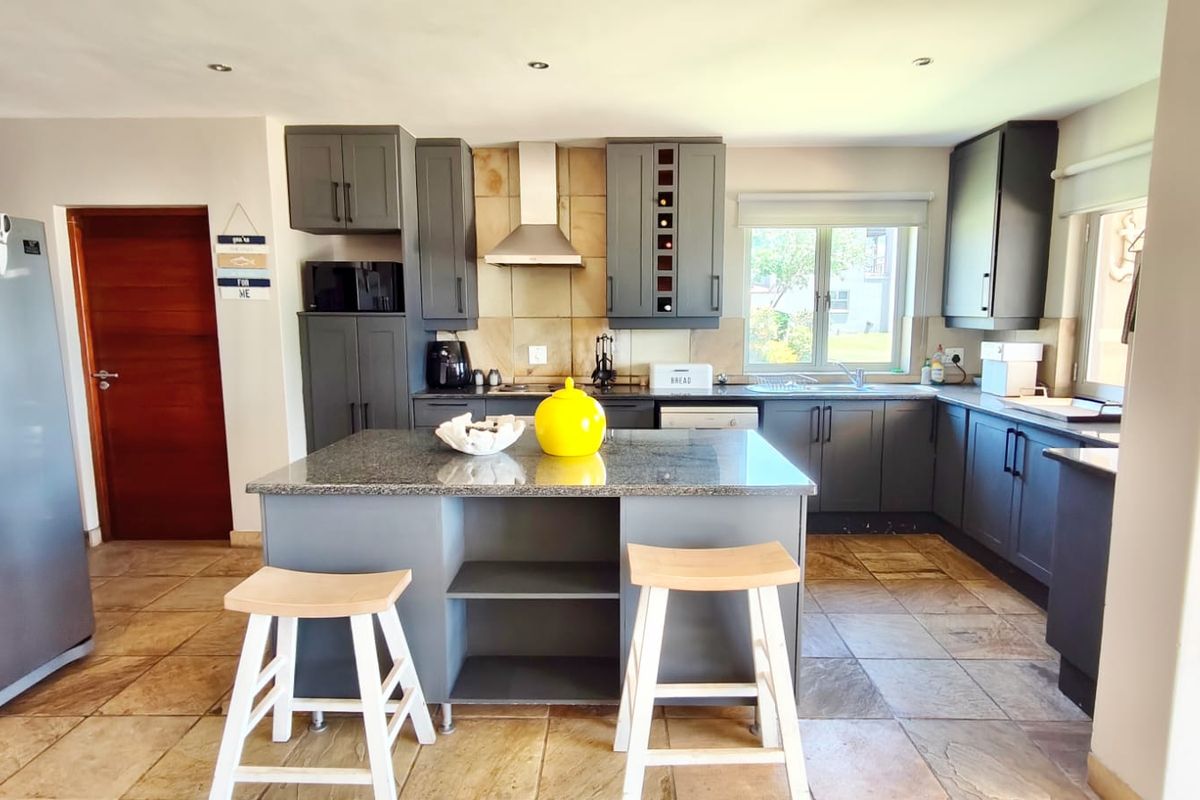 Modern kitchen featuring dark grey cabinetry, granite countertops, a central island, stainless steel extractor fan, and tiled flooring.