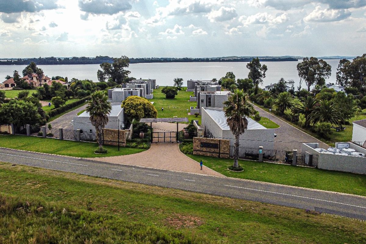Aerial view of a modern residential estate featuring multiple detached units, landscaped grounds, paved driveway, and secure gated entrance overlooking a large lake.