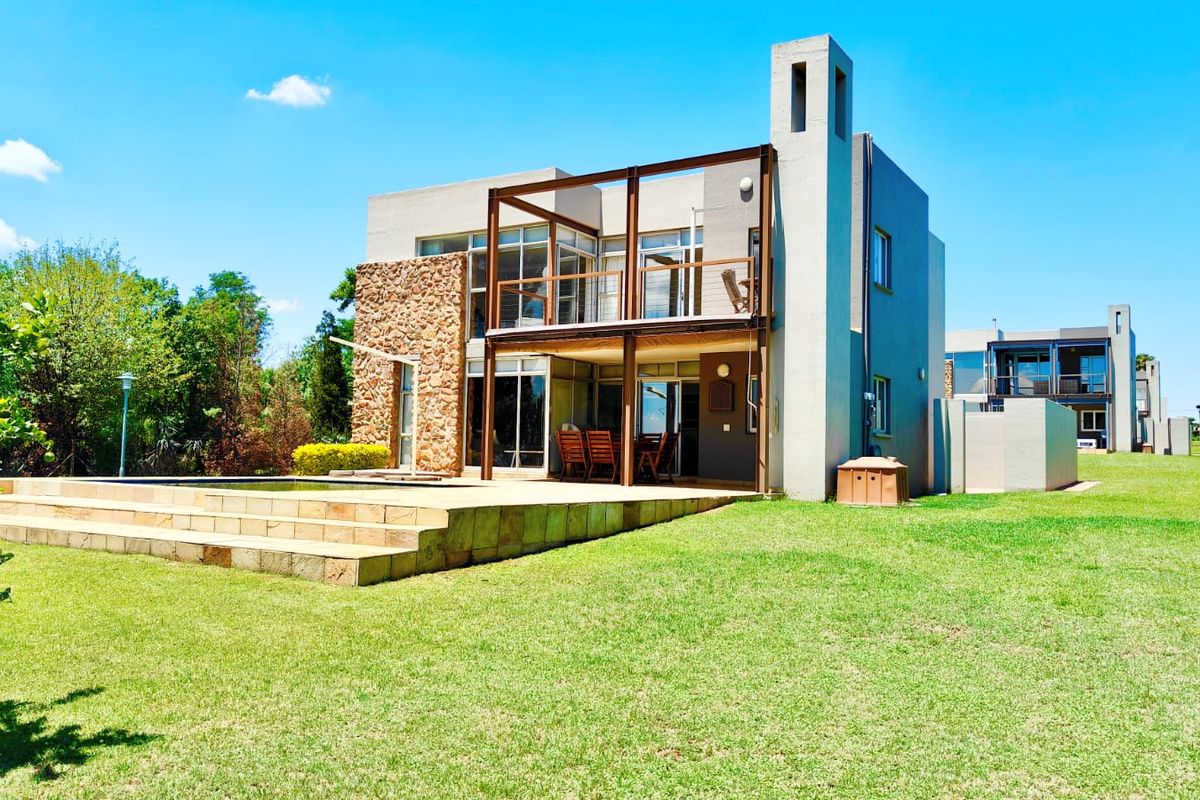 Rear view of a modern two-story house featuring a stone-clad facade, a raised patio deck, a swimming pool, and a balcony.