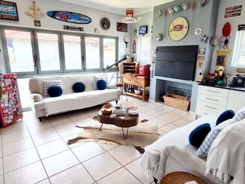 A casual living room featuring large aluminium-framed windows, tiled flooring, and a built-in fireplace with a mantelpiece.