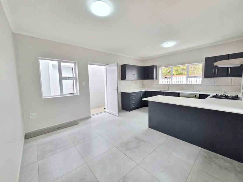Modern kitchen featuring dark cabinetry, stone countertops, gas hob, extractor fan, and tiled flooring, with direct access to an outdoor area.